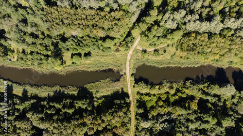 Luftaufnahme von einem Waldweg in der Natur der über einen kleinen Fluss im Wald führt. 