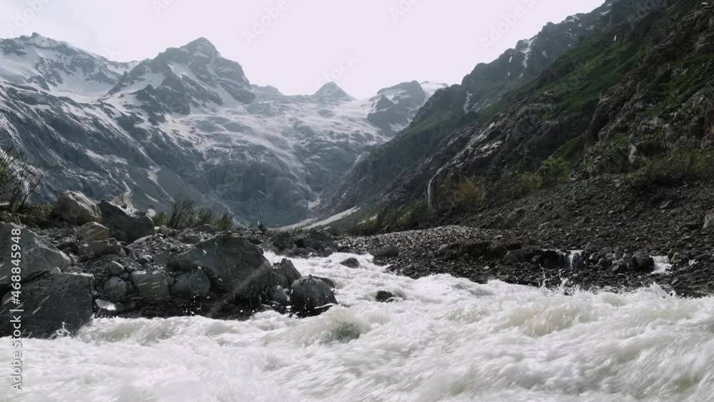 Beautiful landscape with a fast mountain river flowing between rocky stones, splashing water. The waterfall falling from top of mount. Snow and glaciers on caucasus mountain. North Ossetia - Alania Beautiful landscape with a fast mountain river flowing between rocky stones, splashing water. The waterfall falling from top of mount. Snow and glaciers on caucasus mountain. North Ossetia - Alania