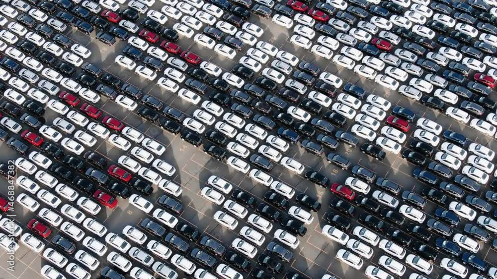 Long rows of finished cars with prevailing white colour at open parking lot of giant factory on sunny day aerial view Long rows of finished cars with prevailing white colour at open parking lot of giant factory on sunny day aerial view