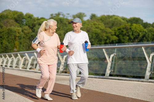 Happy senior couple with bottles runs training together on footbridge