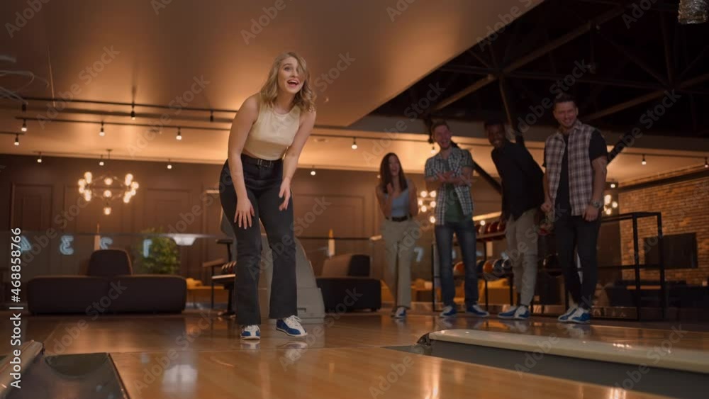 A woman in a bowling alley throws a ball on the track and knocks out a shot in slow motion and