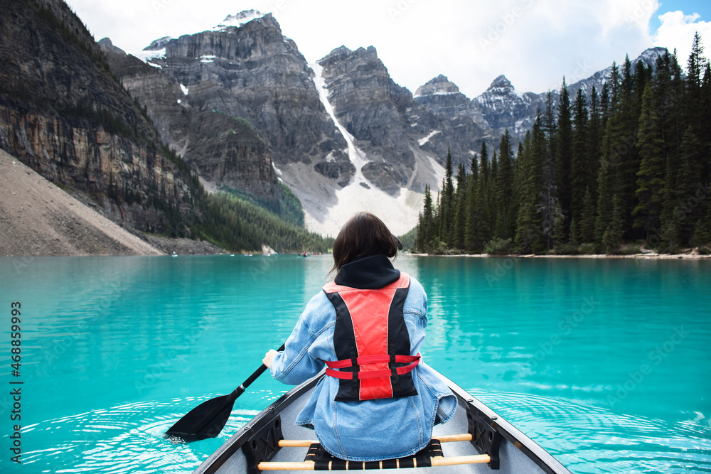 Young girl riding in canoe on turquoise lake with view of mountains
