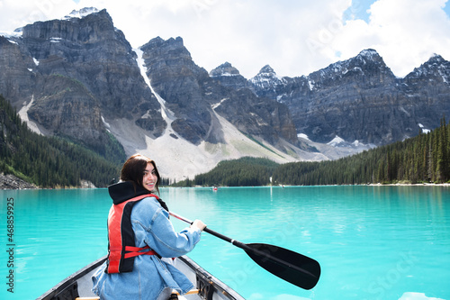 Young girl looking back over shoulder smiling while riding in canoe on turquoise lake with view of mountains
