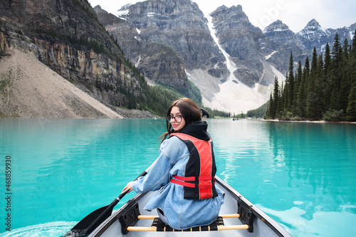 Young girl looking back over shoulder while riding in canoe on turquoise lake with view of mountains