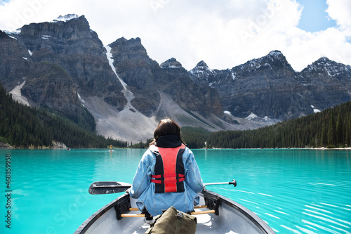 Young girl riding in canoe on turquoise lake with view of mountains