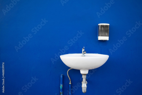 White sink for hand cleaning on blue concrete wall background Wash basin and clear liquid soap dispensers on old concrete wall backgrounds