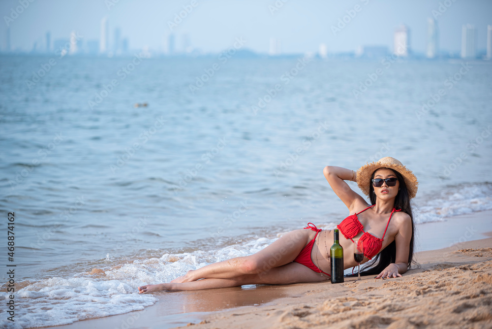 Naklejka premium Beautiful asian woman with long hair wearing glasses and hat lying pose on the beach