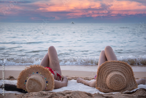 Two young women in straw hats lying on a tropical beach