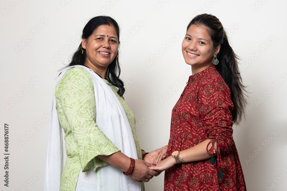 Young Indian girl posing with her mother and looking into the camera. Mother and daughter concept. Daughter celebrating mother's day. Captured in white isolated background. Young Indian girl posing with her mother and looking into the camera. Mother and daughter concept. Daughter celebrating mother's day. Captured in white isolated background.