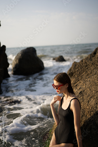 woman in swimsuit sunglasses ocean rocks posing