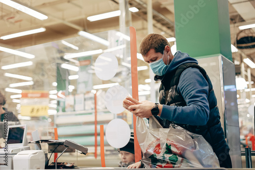 Man in protective medical mask buying food at grocery store or supermarket during quarantine, lockdown, coronavirus pandemic. © Татьяна