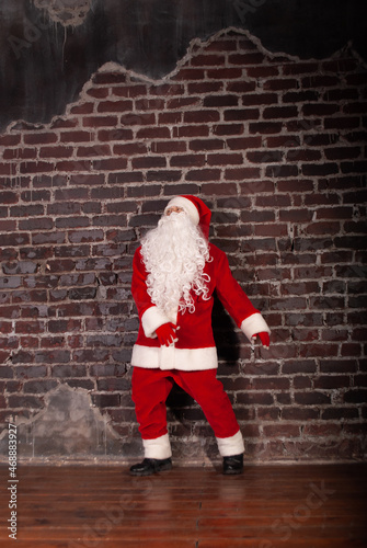 a man in a Santa Claus costume dancing against the background of a brick wall for the New Year and Christmas holidays