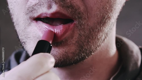 Close up of a young bearded man puts red lipstick on his lips. Man getting makeup. Lgbt concept