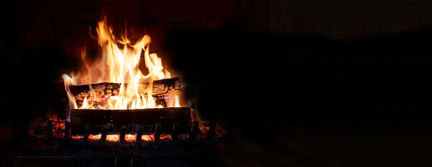 Fireplace burning firewood, fire flames on wood logs, black background. Cozy warm home at Christmas