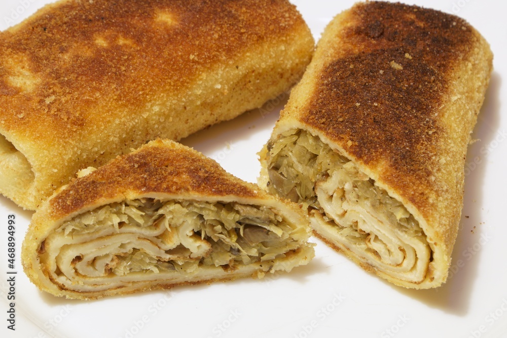 cut croquette with cabbage and mushrooms lying on a white plate next to the whole croquet cut croquette with cabbage and mushrooms lying on a white plate next to the whole croquet