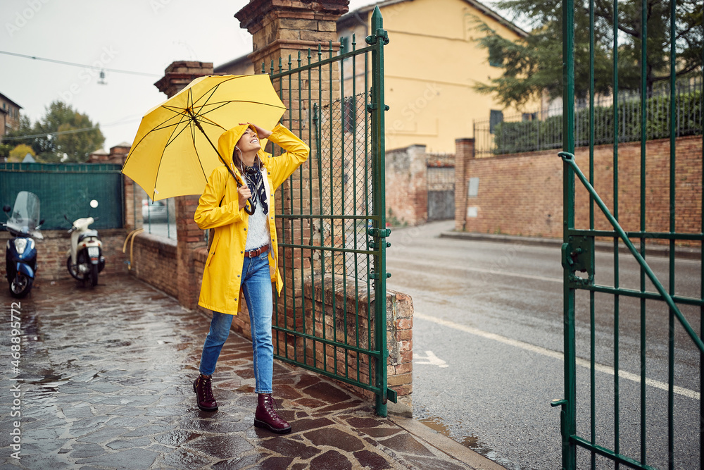 A young girl with yellow raincoat and umbrella is going out for a walk on the rain. Walk, rain, city