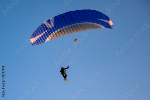 Silhouette of a man on a paraglider flying in the blue sky.