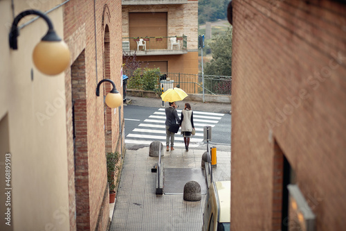 A young couple is crossing the street while walking the city on a rainy day. Walk, rain, city, relationship