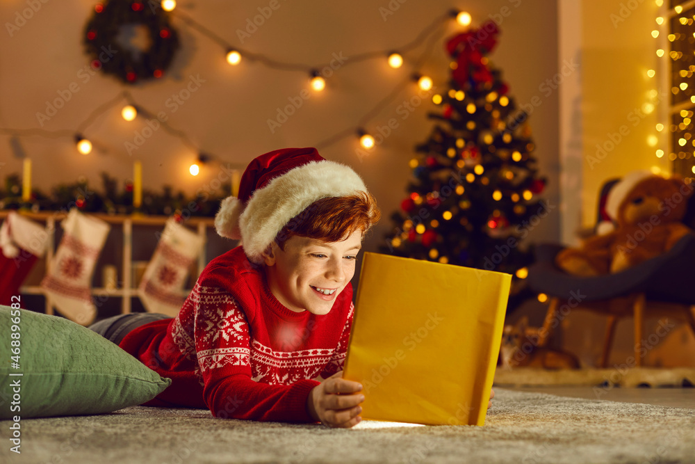 Christmas miracle. Happy boy lies on the floor in a cozy room and reads fairy tales looking at a book that glows with a magical light inside. Concept of a happy childhood. Christmas background. Christmas miracle. Happy boy lies on the floor in a cozy room and reads fairy tales looking at a book that glows with a magical light inside. Concept of a happy childhood. Christmas background.
