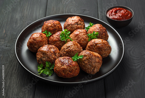 Fried Meatballs in close-up in a black plate on a dark background with tomato sauce.