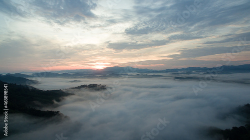 aerial view scenery sunrise mist above the mountain in tropical rainforest..slow floating fog blowing cover on the top of mountain look like as a sea of mist.