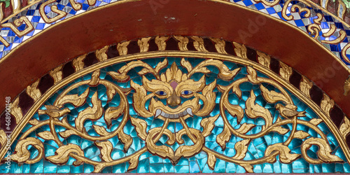 Detail of gilded stucco on glass mosaic representing Kala aka kirtimukha  a guardian and protector deity above entrance of Wat Chiang Man vihara  the oldest buddhist temple in Chiang Mai  Thailand
