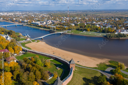 Panoramic aerial view of the Kremlin in Veliky Novgorod, golden autumn in the city, yellow treetops, a bridge over the Volkhov river, city sandy beach, a fortress.
