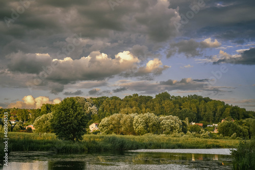 a small village is on the shore of a lake, beautiful contrasting clouds in the sky, evening light, nature of Russia