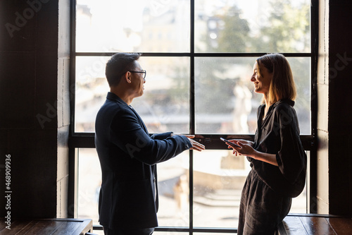 Fotografie Side view of asian man and caucasian woman talking in cafe or coworking near window