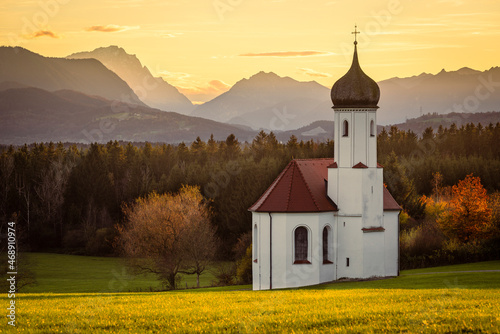 Die Kapelle St. Johann oberhalb des Loisachtals, dem Kochelsee und den herbstlichen bayrischen Alpen in der Abendsonne, Deutschland
