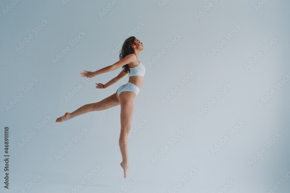 girl gymnast, in a white uniform, panties and top, in the studio on a white background shows exercises girl gymnast, in a white uniform, panties and top, in the studio on a white background shows exercises