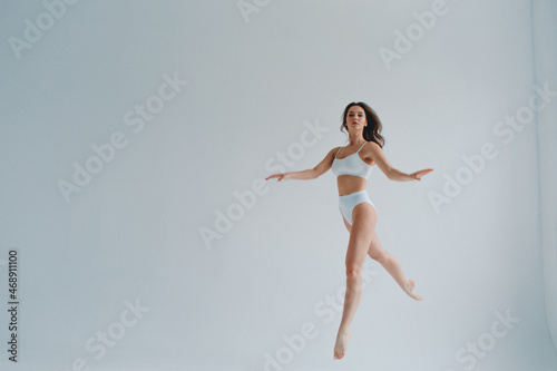 girl gymnast, in a white uniform, panties and top, in the studio on a white background shows exercises