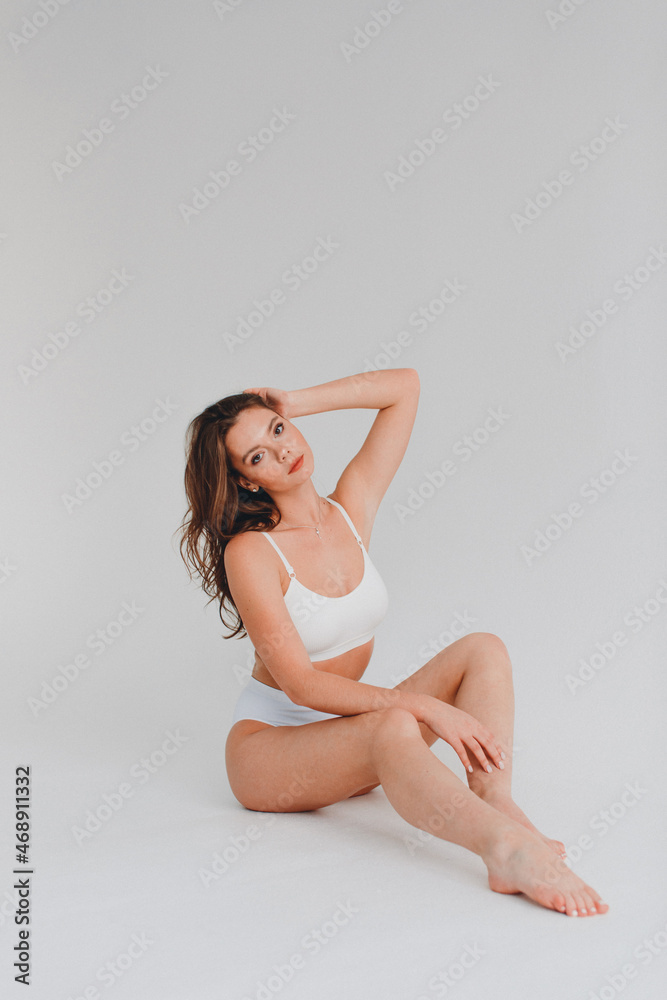 Fototapeta premium girl gymnast, in a white uniform, panties and top, in the studio on a white background shows exercises
