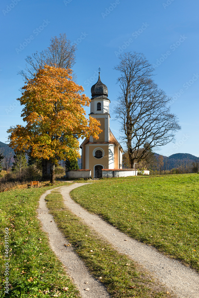 Die barocke Kirche St. Margareth auf der Halbinsel Zwergern im Walchensee mit herbstlich gefärbten Bäumen, Bayern, Deutschland
