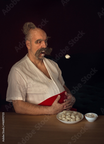Funny man dressed like cossack is eating flying russian dumplings. Image with selective focus and toning photo