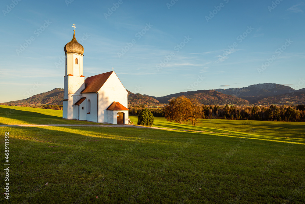 Die Kapelle St. Johann oberhalb des Loisachtals, dem Kochelsee und den herbstlichen bayrischen Voralpen in der Abendsonne, Deutschland