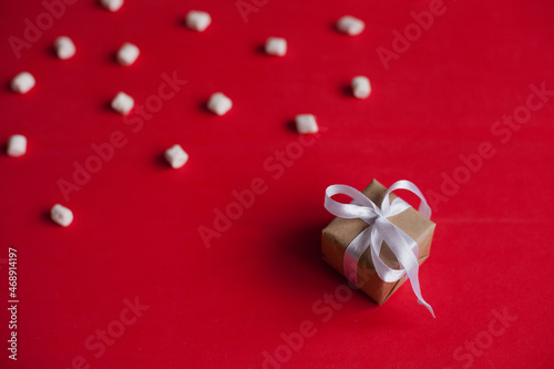 small gift box with white ribbon on red background with marshmallows minimal shot