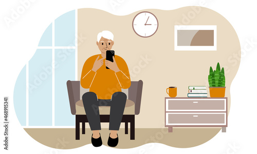 Grandpa holds a mobile phone in his hand and sits on an armchair at home. An elderly man is learning to use the telephone.