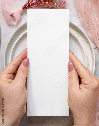 Hand with menu card with pink flowers and ribbons over wedding table place photo