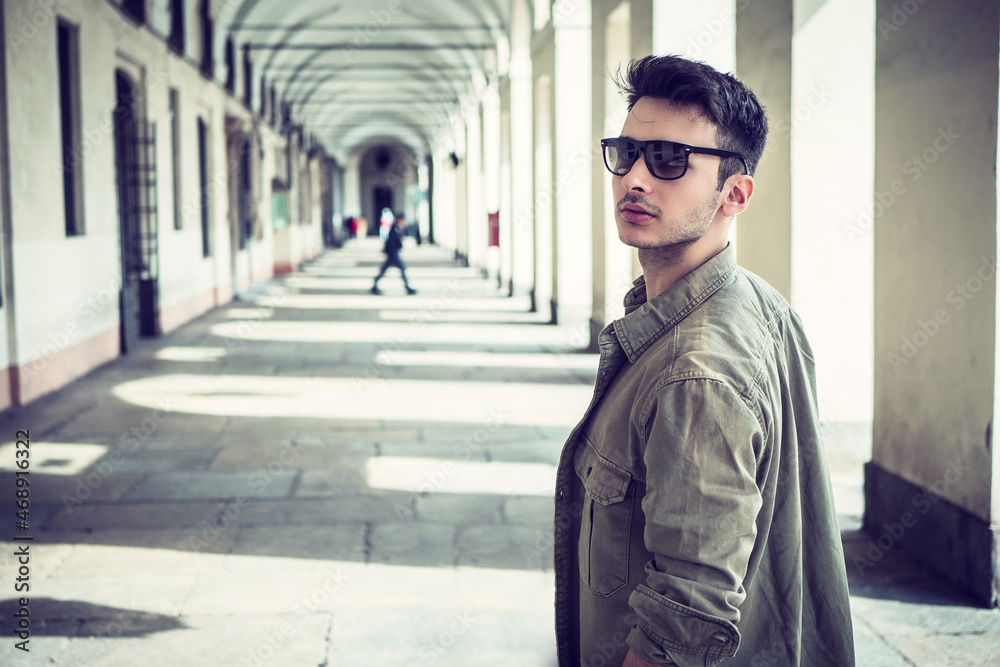 Attractive young man outdoor wearing jacket and sunglasses, under colonnade