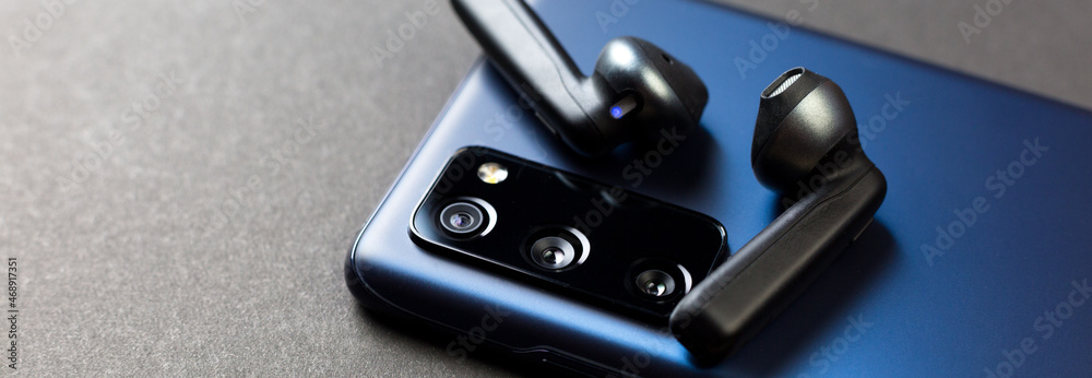 Naklejka premium Modern gadgets, smartphone and wireless headphones on a dark background, close-up.