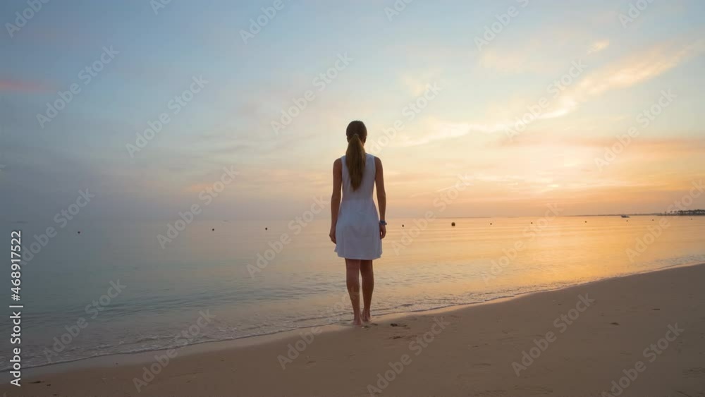 Lonely young woman standing on sandy beach by seaside enjoying warm tropical evening Lonely young woman standing on sandy beach by seaside enjoying warm tropical evening