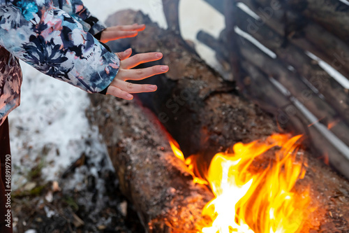 The girl warms her hands over the fire. Burning logs in the snow.