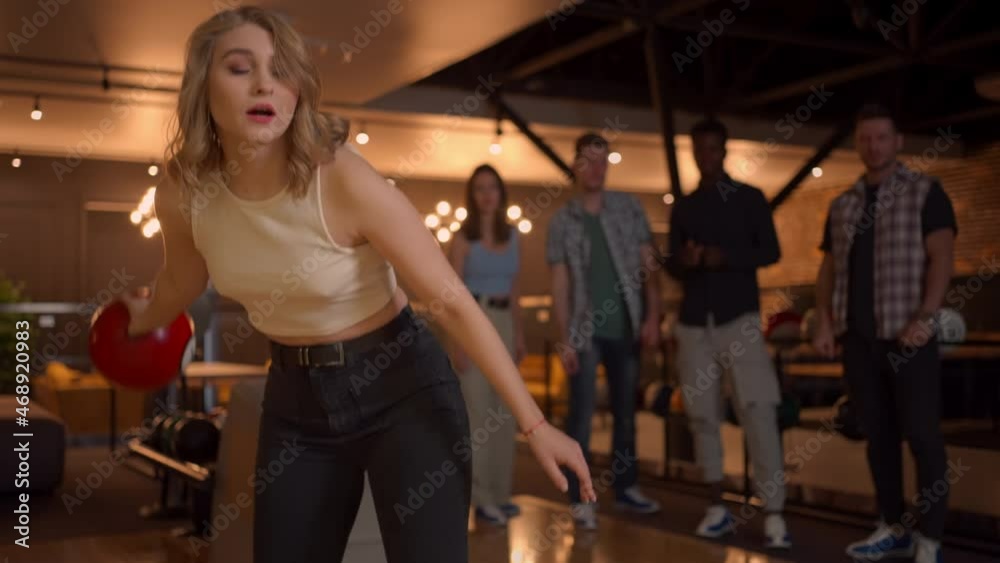 Portrait of a young woman throwing a bowling ball and knocking out a shooter who jumps and dances with joy in slow motion