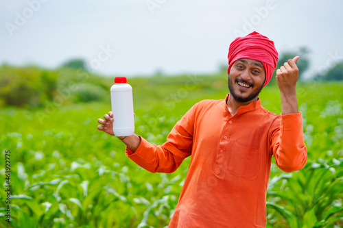 Young indian farmer showing liquid fertilizer bottle at agriculture field.