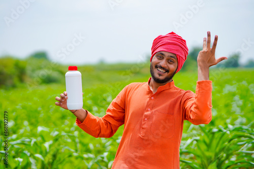 Young indian farmer showing liquid fertilizer bottle at agriculture field.