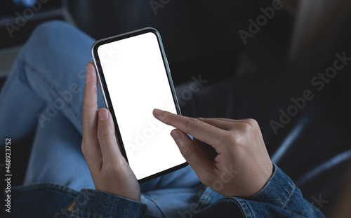 Cell phone mockup image blank white screen. Woman hand holding, using mobile phone during working on laptop computer at home. . empty space for advertise text.