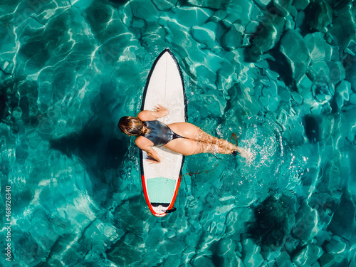 Surf girl relax on surfboard in transparent ocean. Aerial view with surfer woman