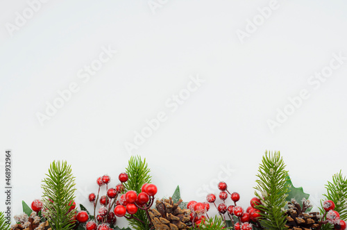 White background with a Christmas ornament of spruce branches  cones and holly. Space for text. High quality photo.
