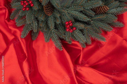 Christmas tree branches with red winter berries and pine cone on red silk or satin background